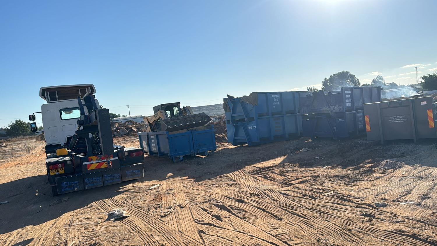 מגרש מכולות עם משאית ובובקט ומכולות כחולות מסודרות