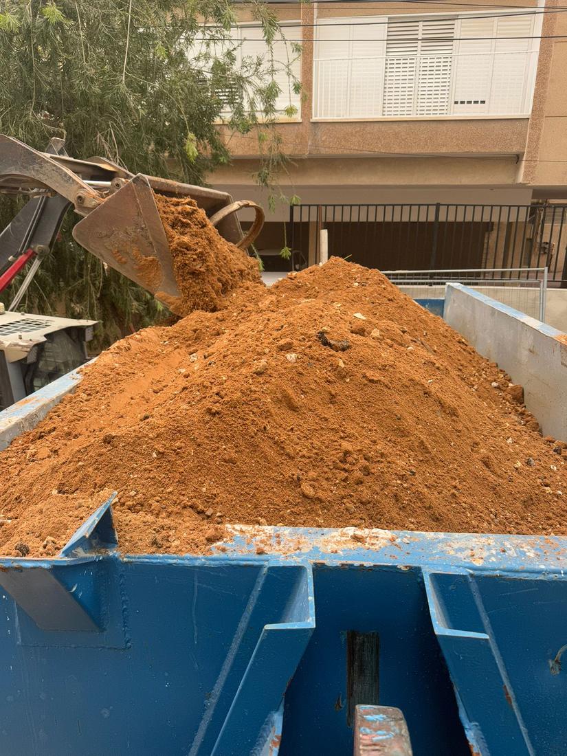 שופל מעמיס עפר כתום לתוך מכולה כחולה ברחוב מגורים