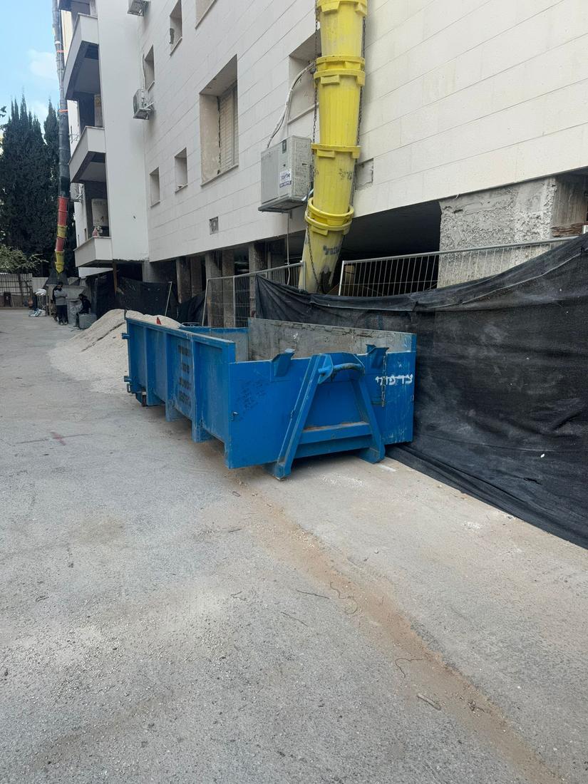 מכולה כחולה ריקה מתחת לשרוול פסולת צהוב באתר התחדשות עירונית
