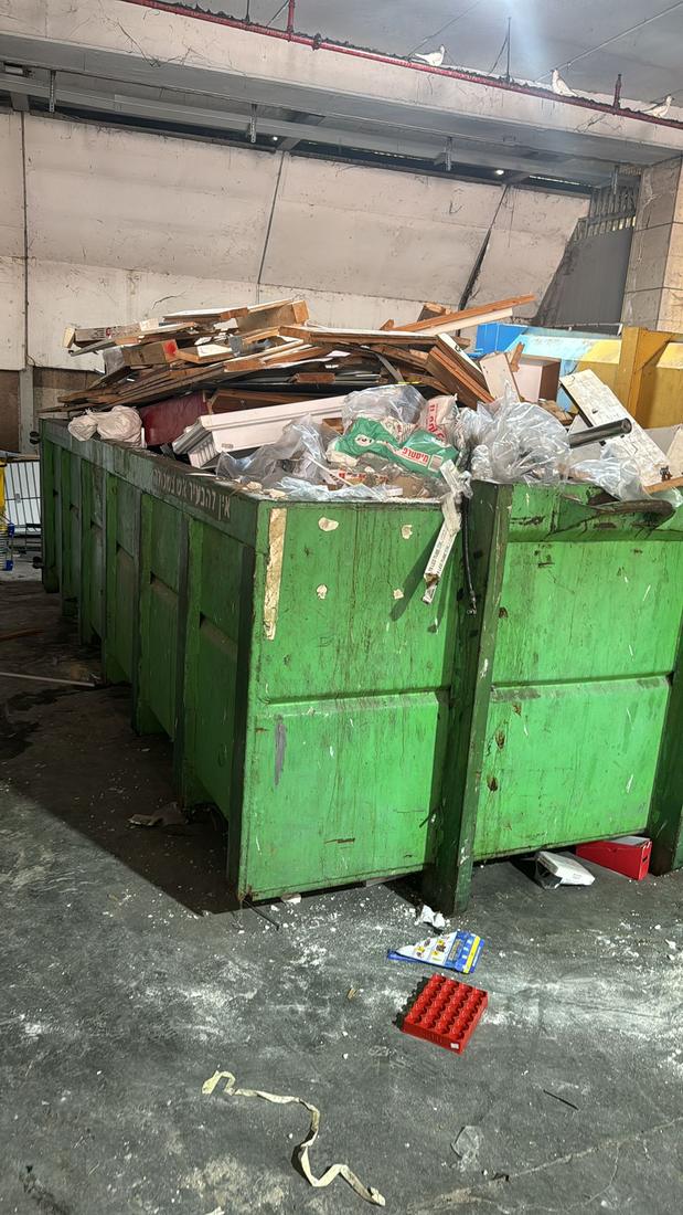 מכולות ירוקות מלאות בפסולת עץ וגבס בחניון תת־קרקעי